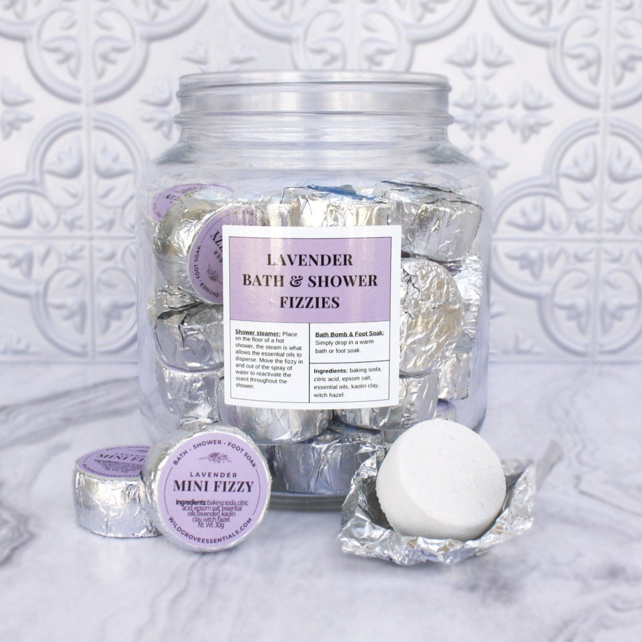 Glass jar of Lavender scented bath and shower fizzies wrapped in foil with purple labels.