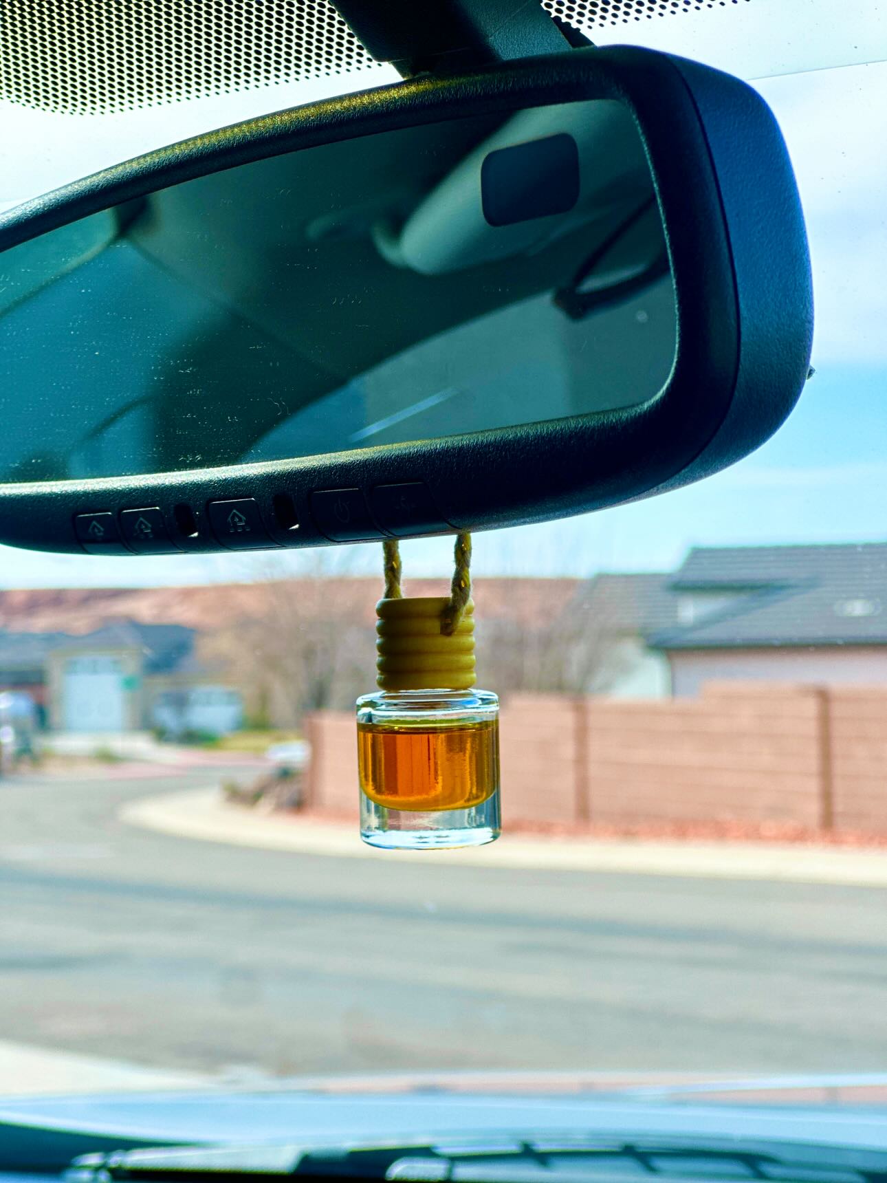 glass car freshener bottle with wood cap hanging from a rearview mirror of a car