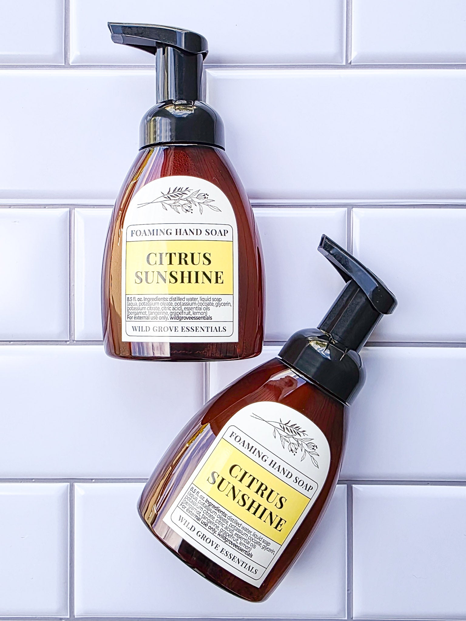 2 bottles of Citrus Sunshine scented foaming hand soap in amber bottles on a white tile background