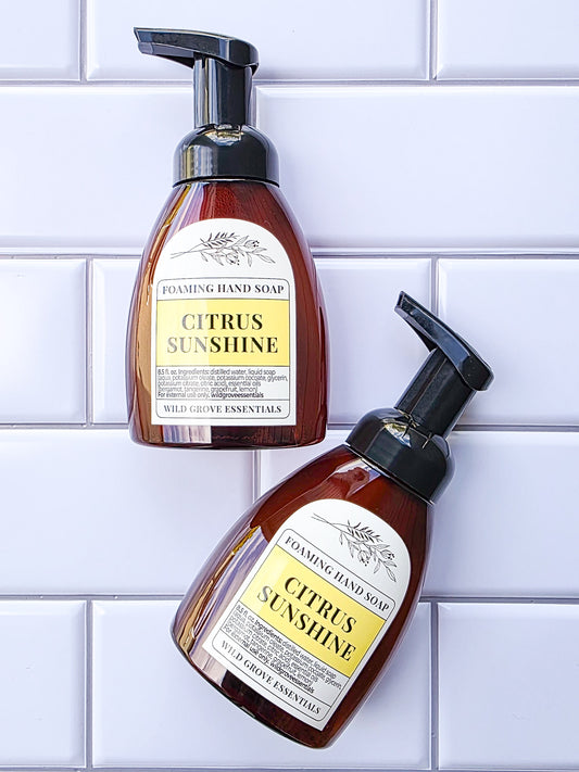 2 bottles of Citrus Sunshine scented foaming hand soap in amber bottles on a white tile background