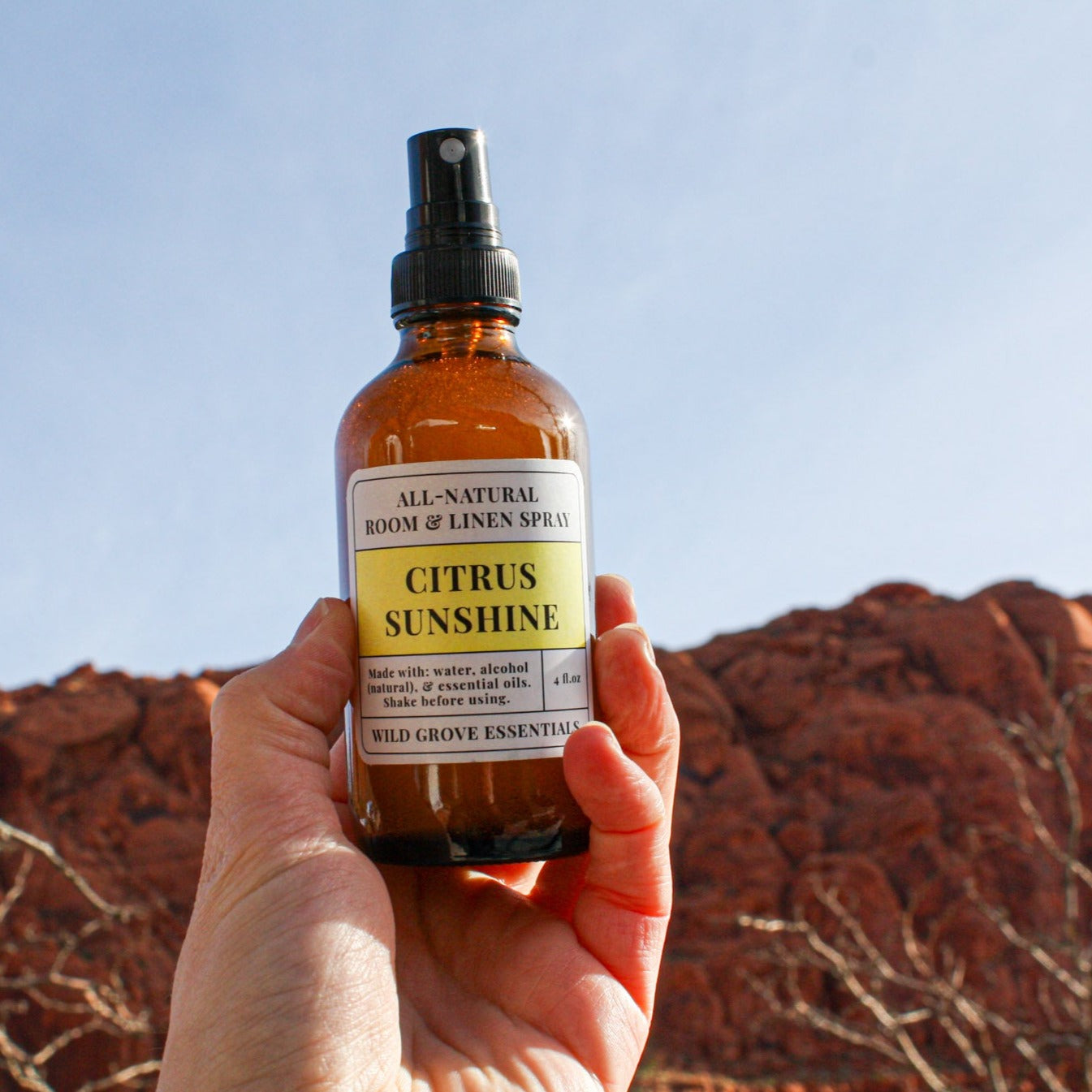 Room and linen spray bottle in 4oz amber bottle in Citrus Sunshine against a clear blue sky and red rocks. 