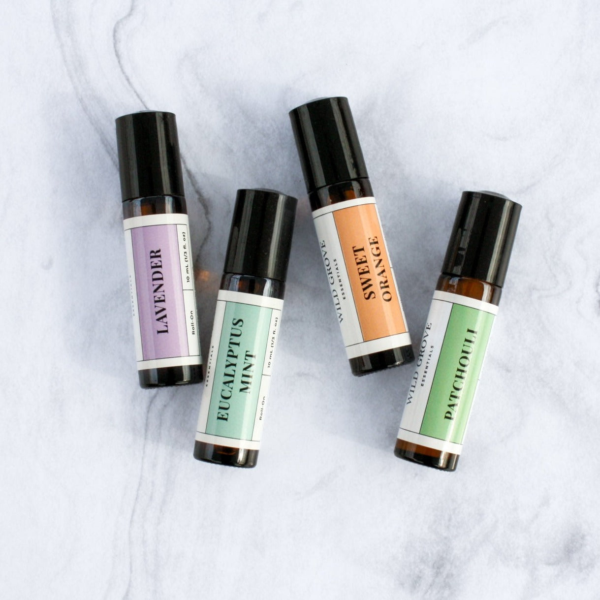 4 essential oil roll-on bottles each in 10ml amber bottle on a marble backdrop in Patchouli, Sweet Orange, Eucalyptus Mint, and Lavender scents.