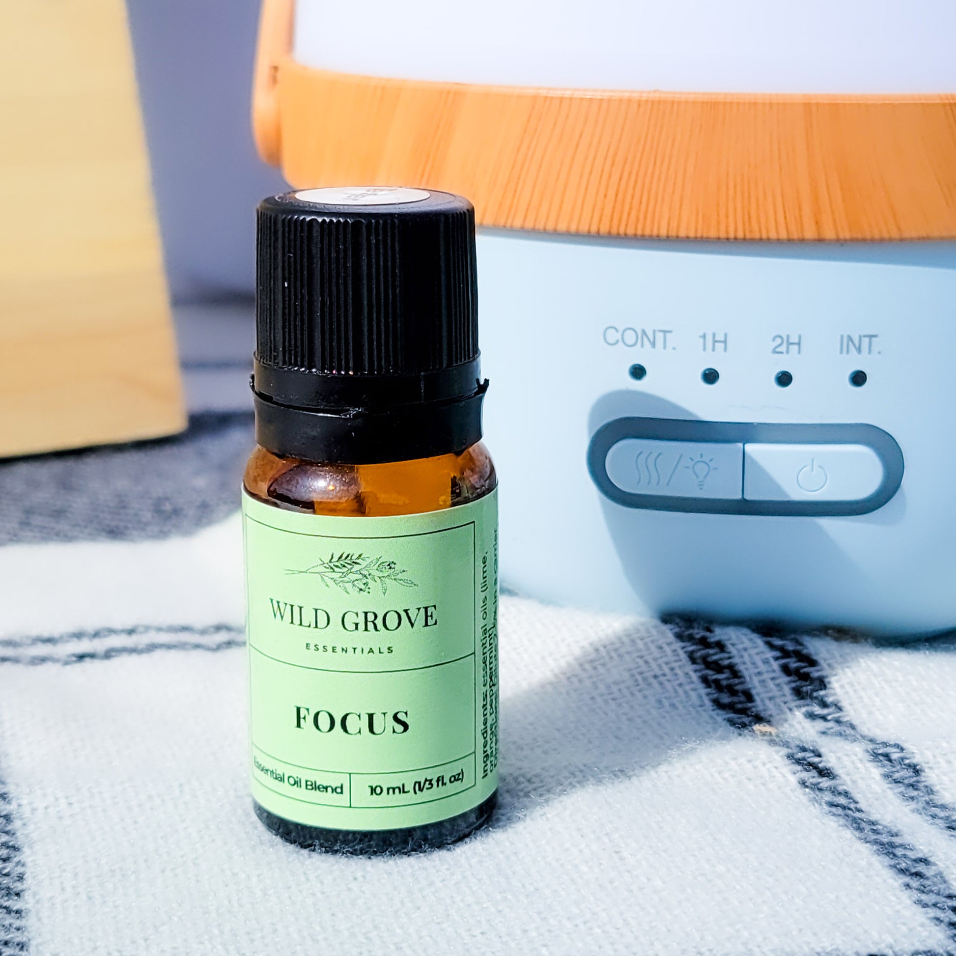 A bottle of Focus essential oil blend in a 10ml bottle set in front of an essential oil diffuser.