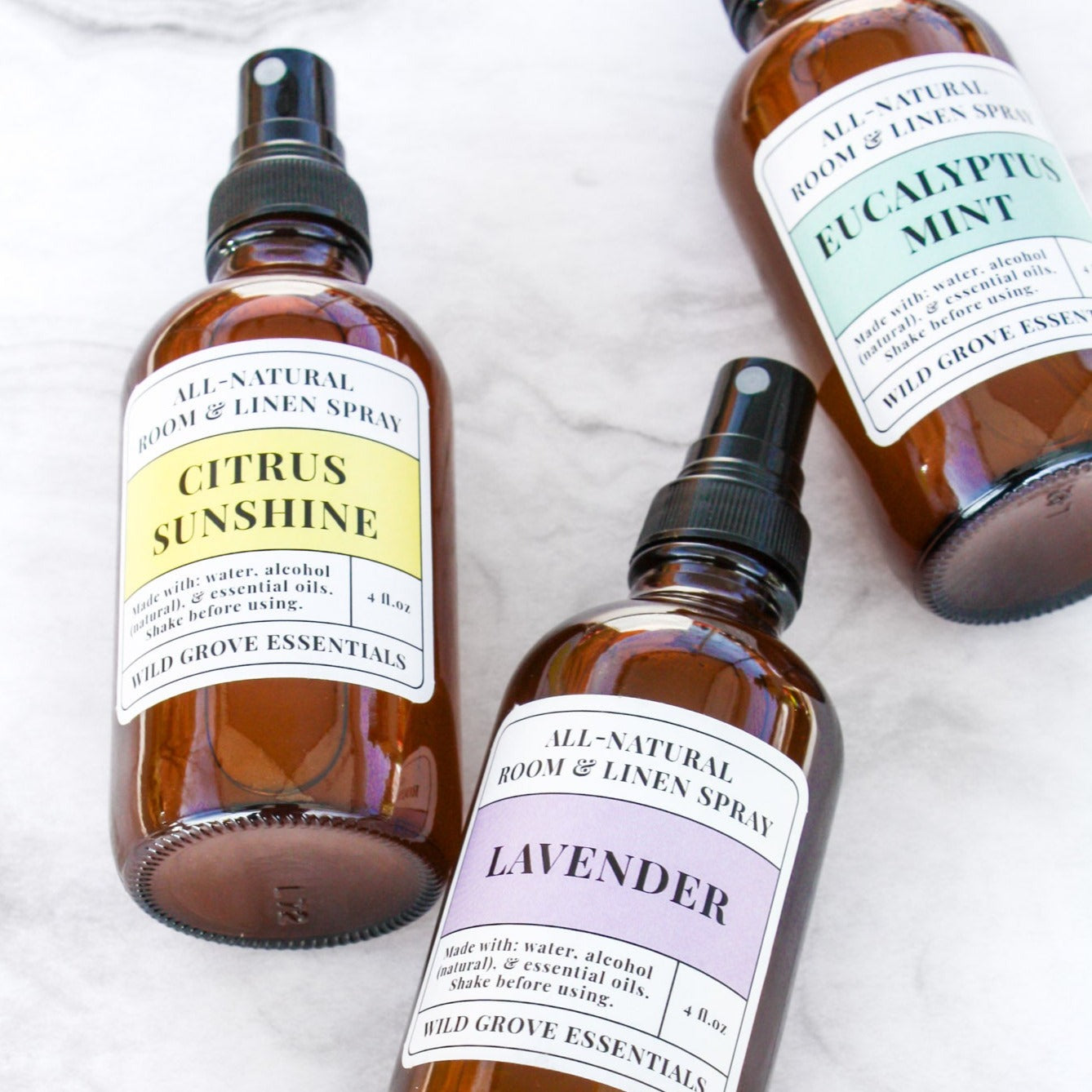 Three room and linen sprays in 4 oz amber glass bottles on a marble backdrop in Citrus Sunshine, Lavender, and Eucalyptus Mint scents.