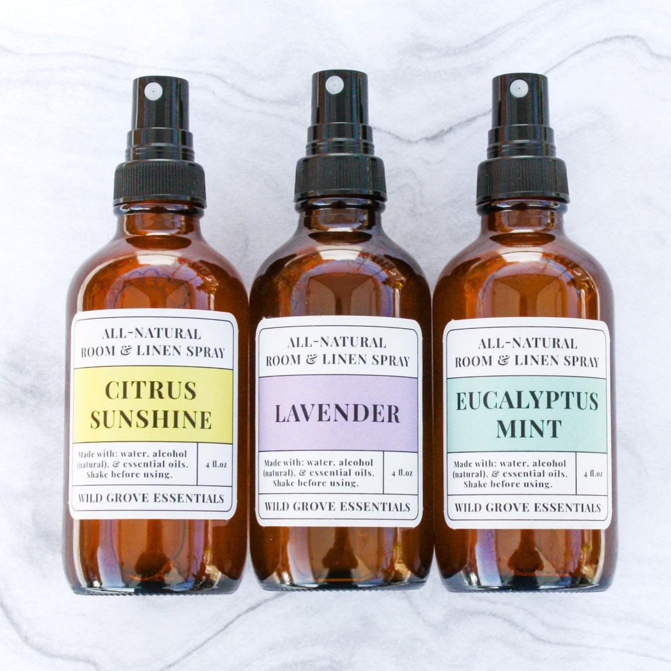 Three room and linen sprays in 4 oz amber glass bottles on a marble backdrop in Citrus Sunshine, Lavender, and Eucalyptus Mint scents.