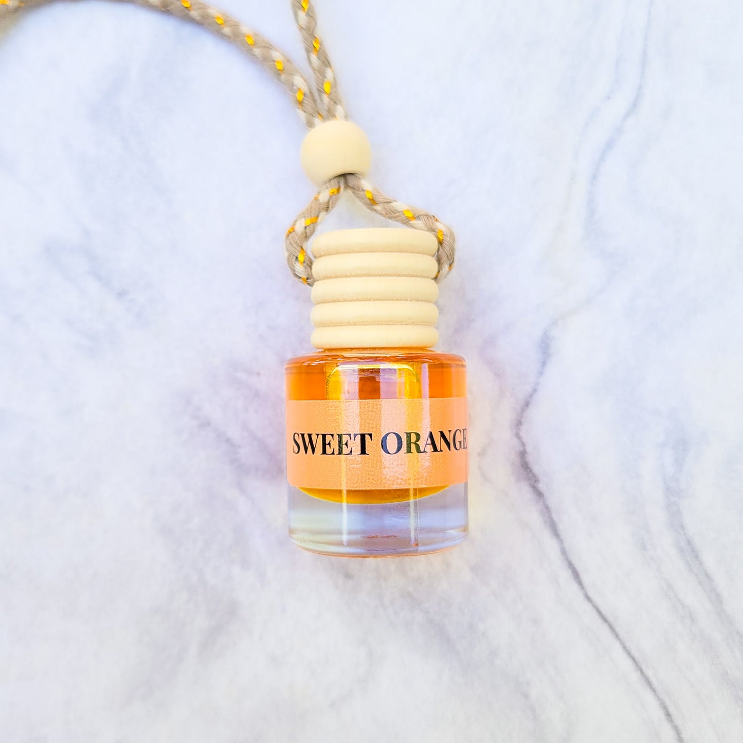 Car freshener in glass bottles with wooden top  Sweet Orange scent laid on a marble backdrop.
