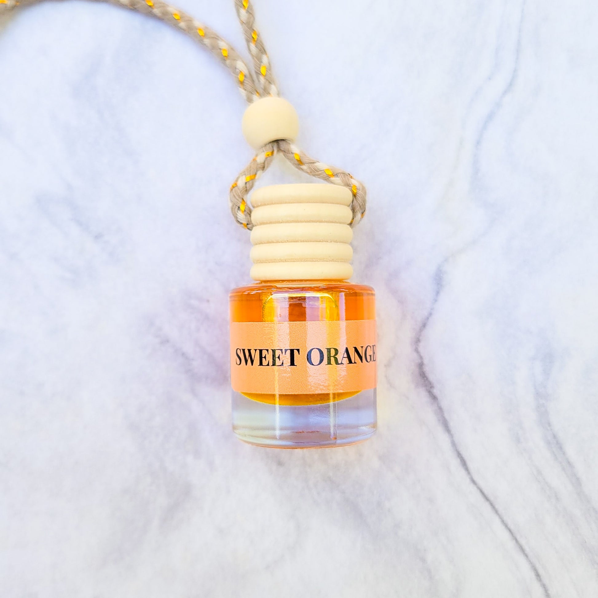 Car freshener in glass bottles with wooden top  Sweet Orange scent laid on a marble backdrop.